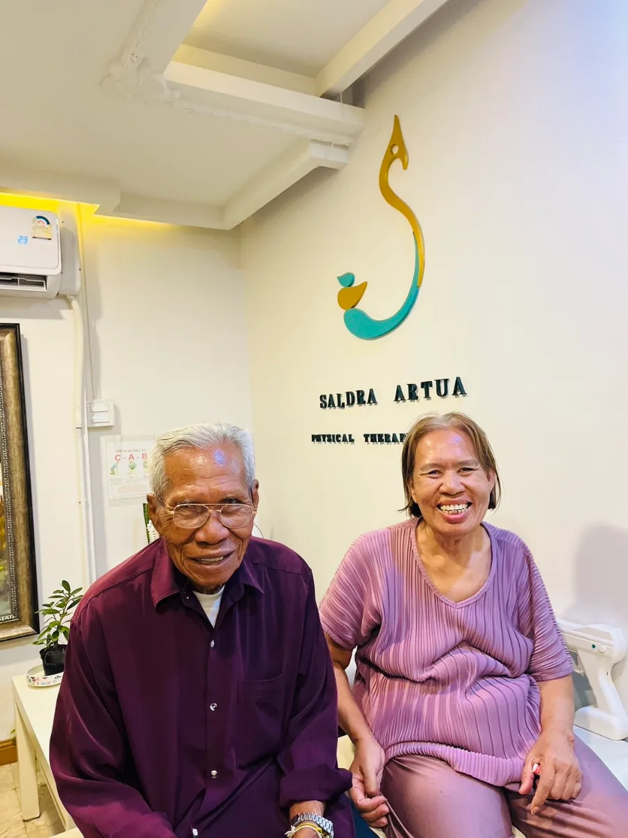 ผู้สูงอายุสองท่านนั่งจับมือกันระหว่างเข้ารับบริการฟื้นฟูที่คลินิก Saldra Artua